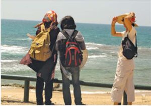 Photo of three women looking out to sea from a sandy beach.